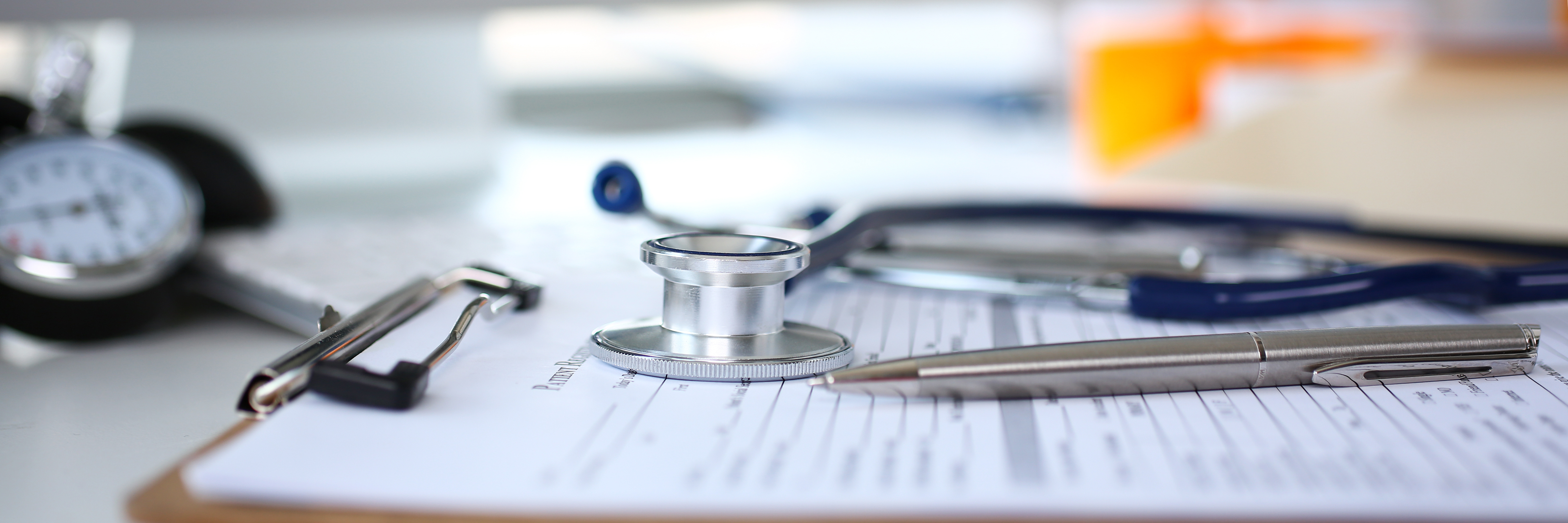A stethescope, a blood pressure gauge, and an ink pen laying on top of a clipboard.